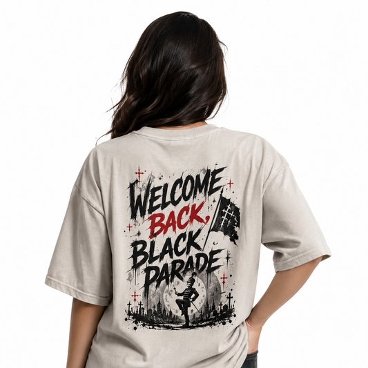 A woman shown from the back wearing a light beige graphic t-shirt with a 'Welcome Back, Black Parade' design in black and red, paired with black cargo pants, against a plain white background.